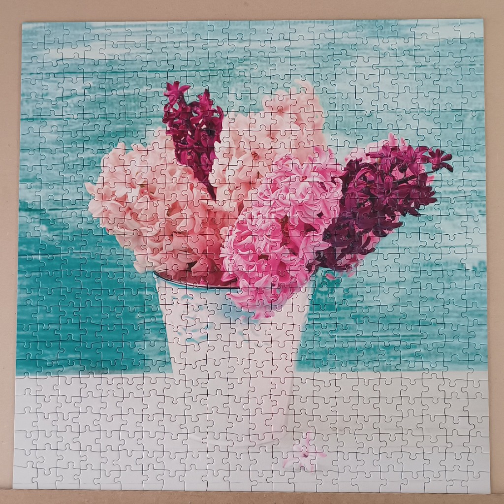 A bouquet of pink and purple hyacinth flowers in a white bucket against a turquoise wooden background.
