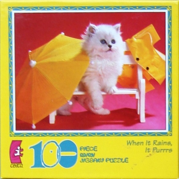 A fluffy white kitten sits on a white bench under a yellow umbrella against a bright red background.