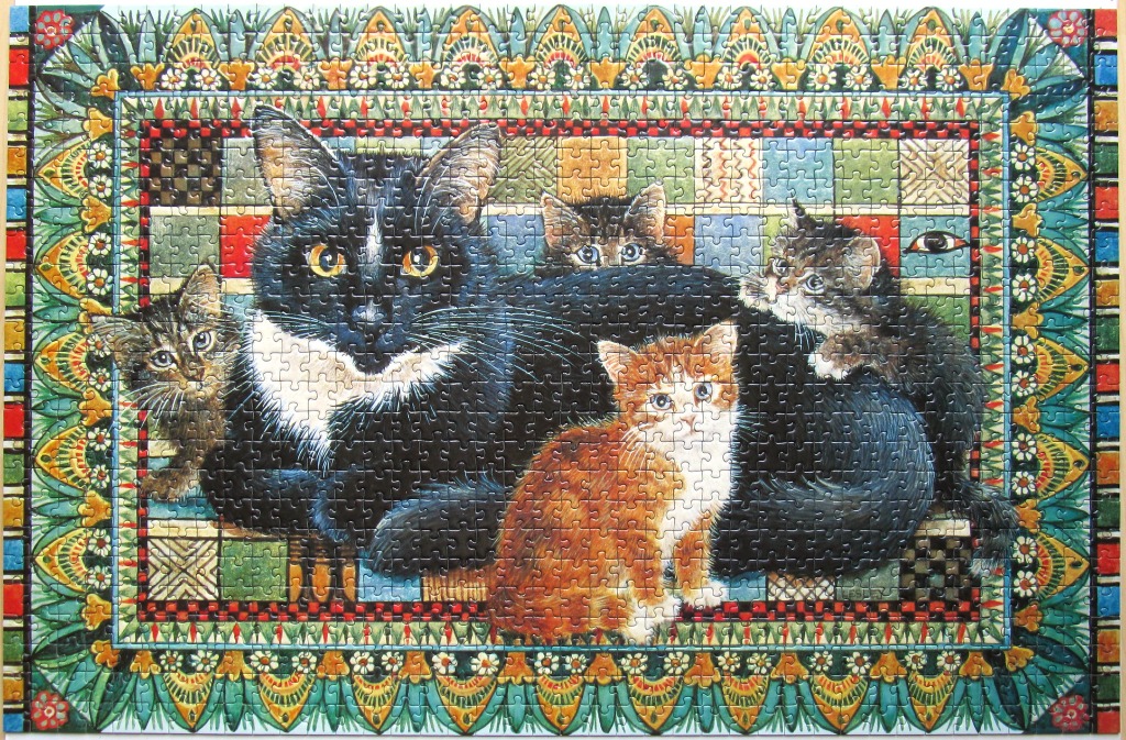 An illustration of a mother cat and her three kittens nestled against a colorful quilt, framed by an ornate border.