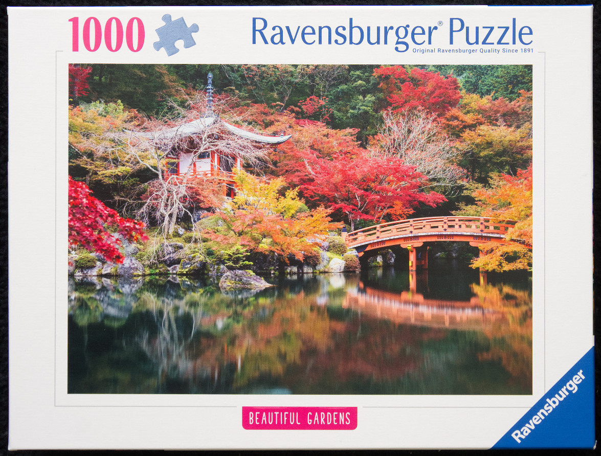 A traditional Japanese pagoda and arched wooden bridge reflected in a calm pond surrounded by vibrant autumn foliage.