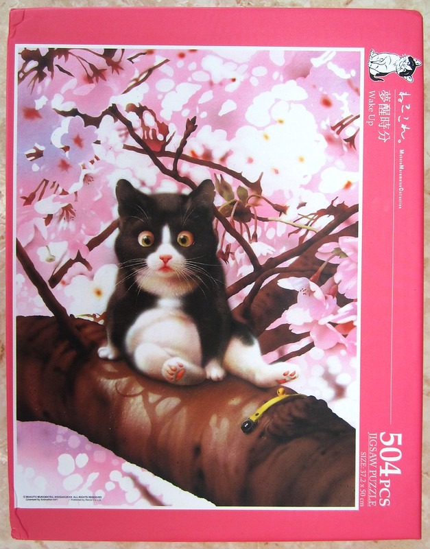 A black and white cat sitting on a large tree branch surrounded by soft pink cherry blossoms.