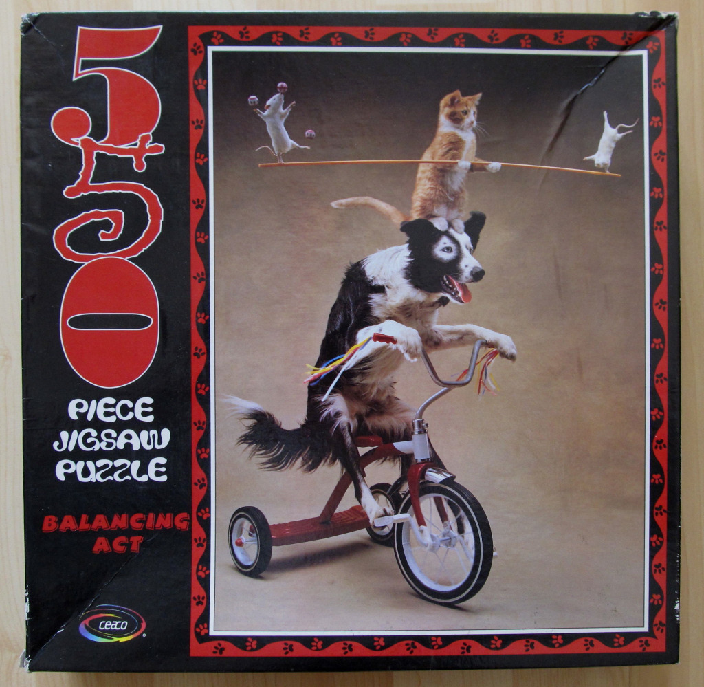 A black and white dog riding a red tricycle with a cat and two mice performing a circus act on its head.