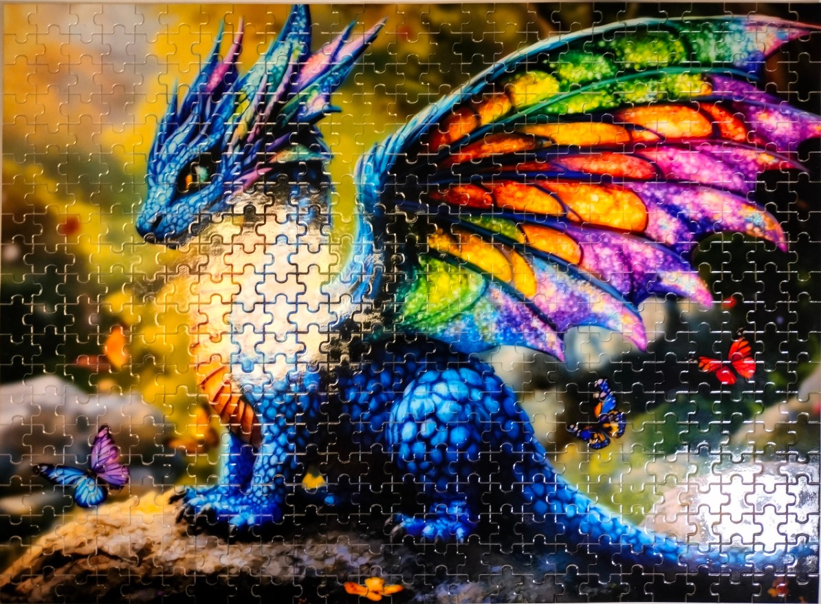A small blue fantasy dragon with vibrant rainbow-colored wings perched on a rock, surrounded by butterflies.