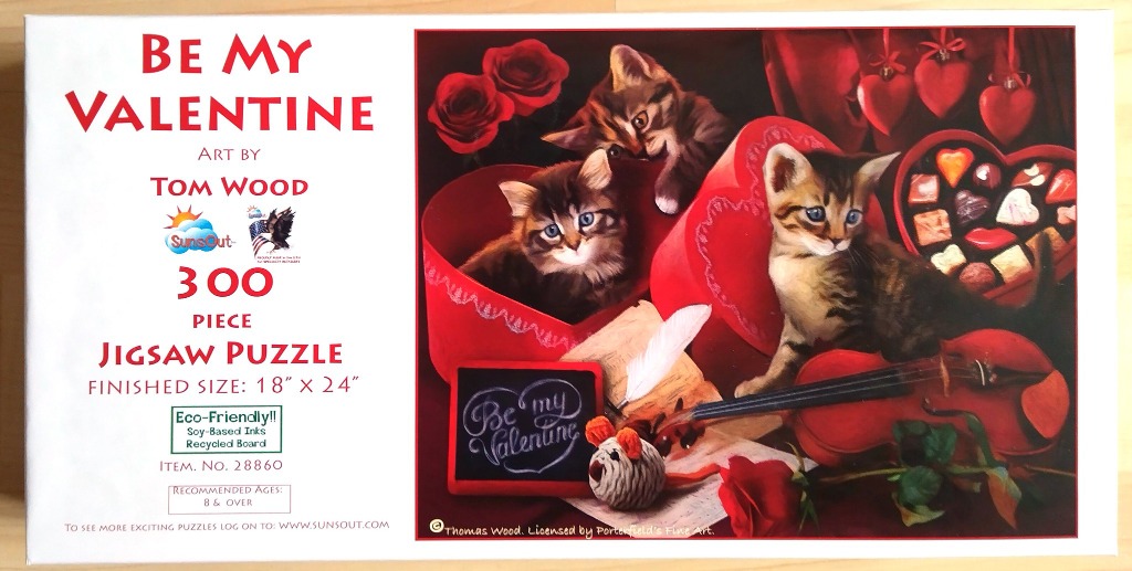 Three kittens sitting with Valentine's Day themed items including a heart-shaped candy box, roses, and a violin.