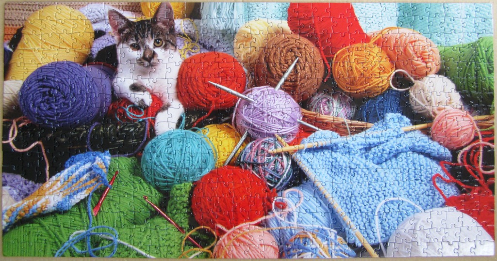 A tabby and white kitten surrounded by a vibrant collection of colorful yarn balls and knitting supplies.