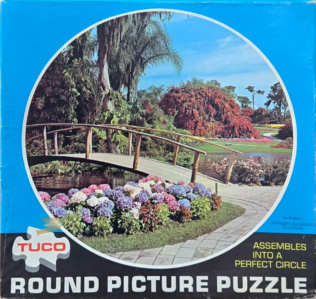 A photograph of a footbridge in a lush, floral garden with hydrangeas in the foreground.