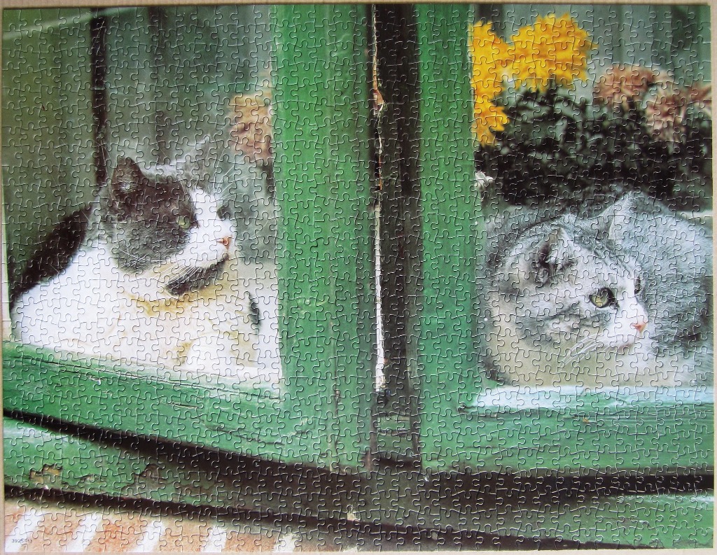 Two cats looking through a green-framed window pane with yellow flowers in the background.