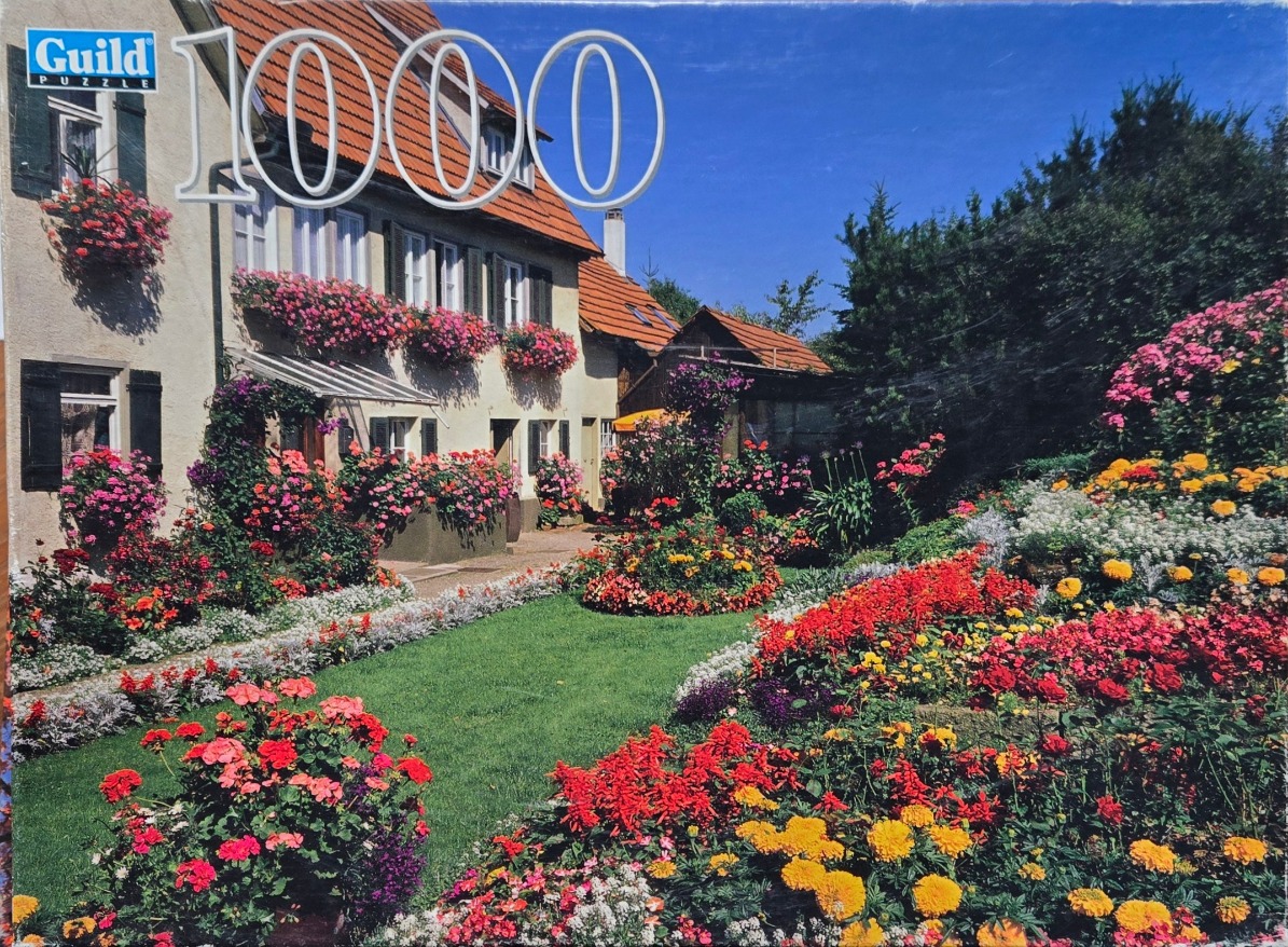 A lush garden in front of a traditional European house with terracotta roof tiles, filled with vibrant blooming flowers.