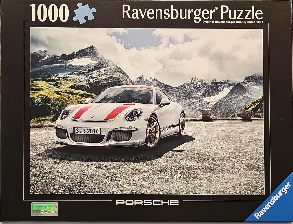 A white Porsche 911 GT3 with red racing stripes parked on an asphalt road in front of snowy mountain peaks.