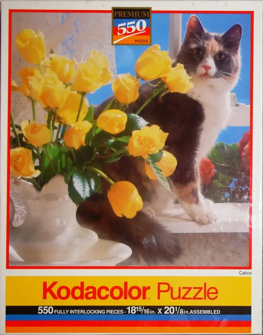 A calico cat sitting on a windowsill next to a vase of bright yellow roses.