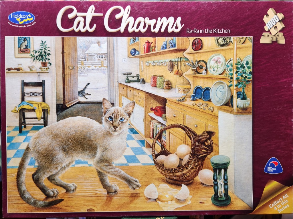 A Siamese cat stands on a wooden kitchen counter next to a basket of eggs and an hourglass.