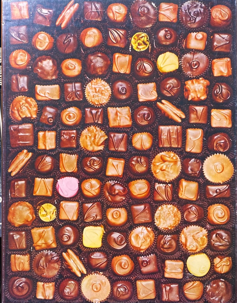 A top-down view of a dense grid of assorted chocolate candies in individual paper cups.