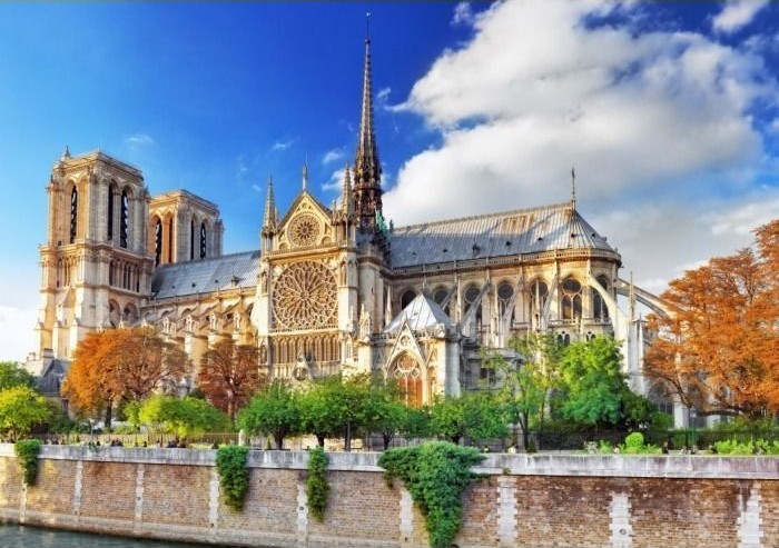 A view of the Notre-Dame Cathedral in Paris with autumn foliage and a bright blue sky