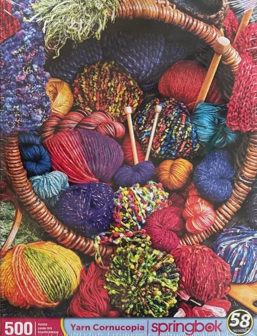 A close-up photograph of a wicker basket overflowing with colorful, textured balls of yarn and wooden knitting needles.