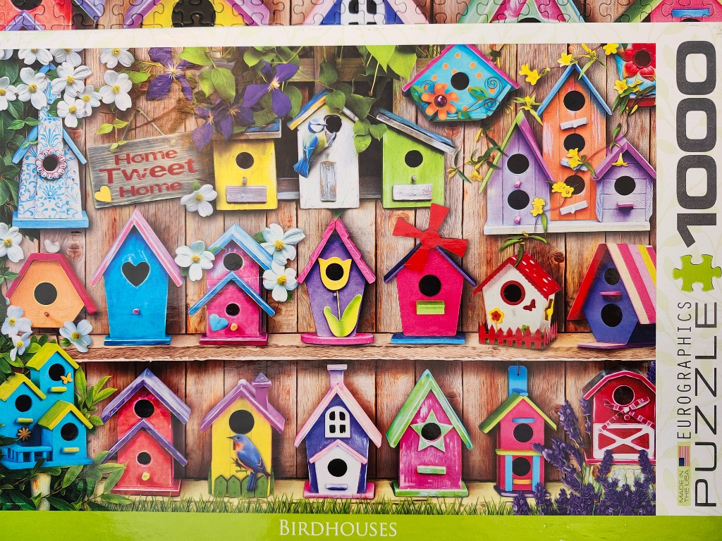 A collection of colorful, whimsically decorated birdhouses hanging on a weathered wooden wall.
