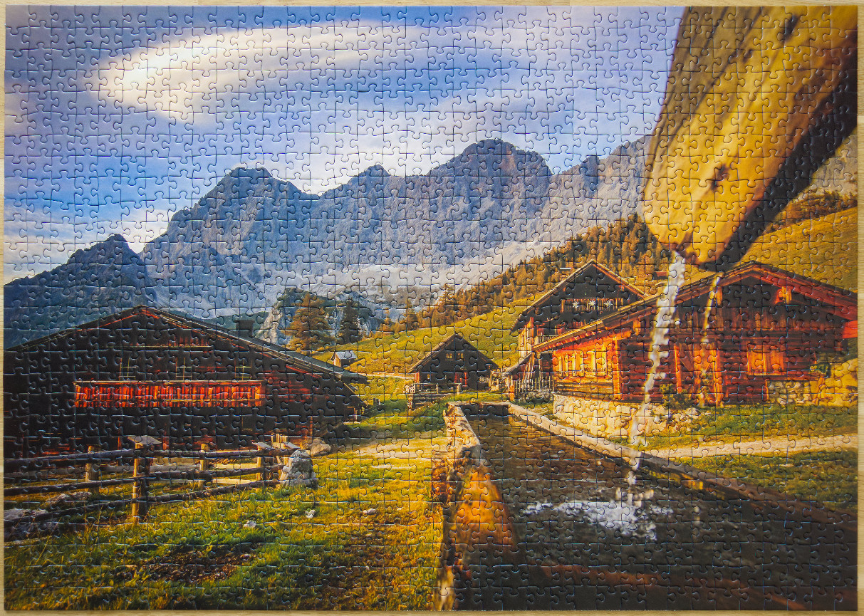 A mountain valley scene with rustic wooden huts and a water trough flowing under a jagged mountain range.