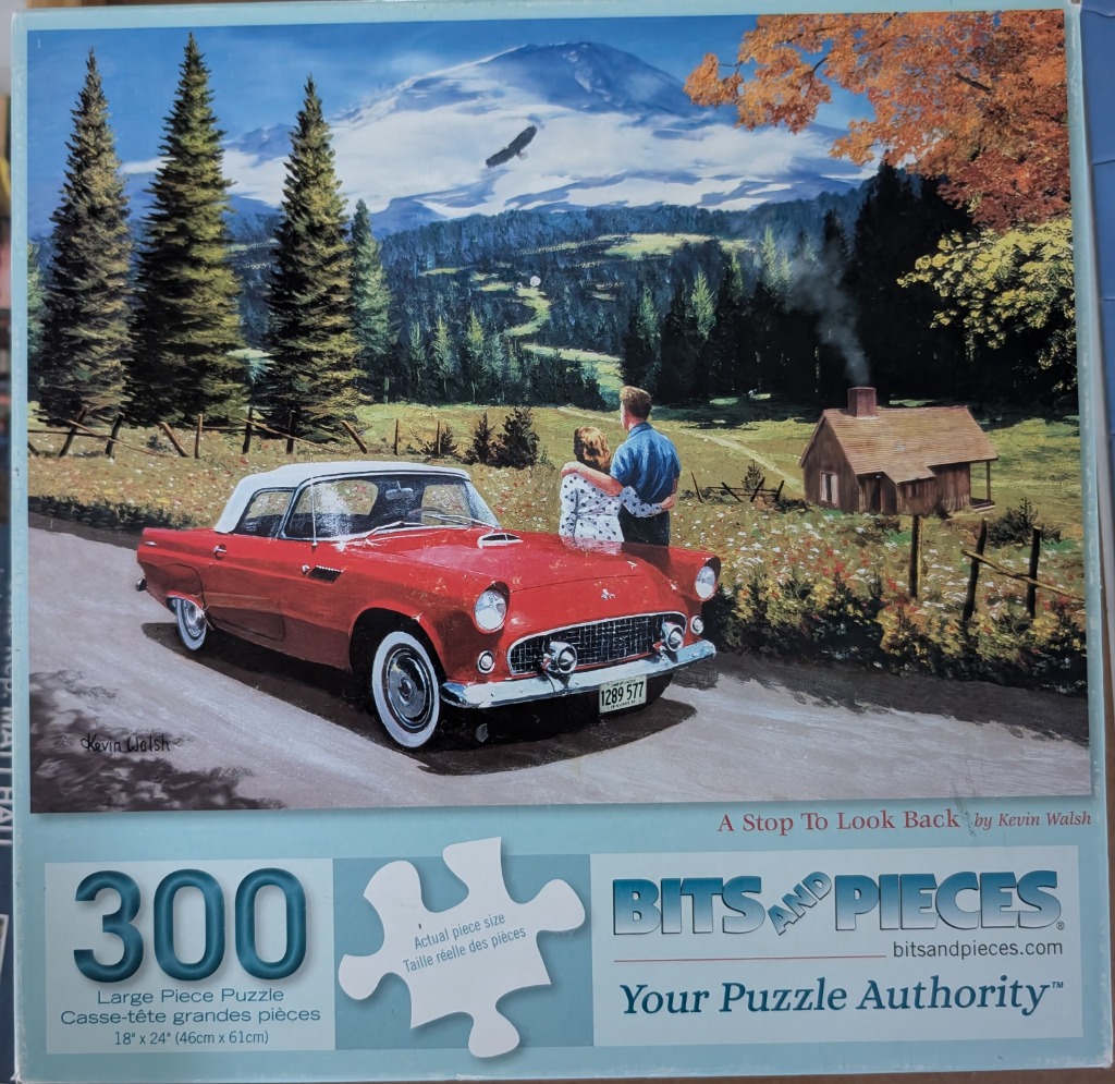 A red classic convertible car parked on a road with a couple looking at a mountain landscape and a small wooden cabin.