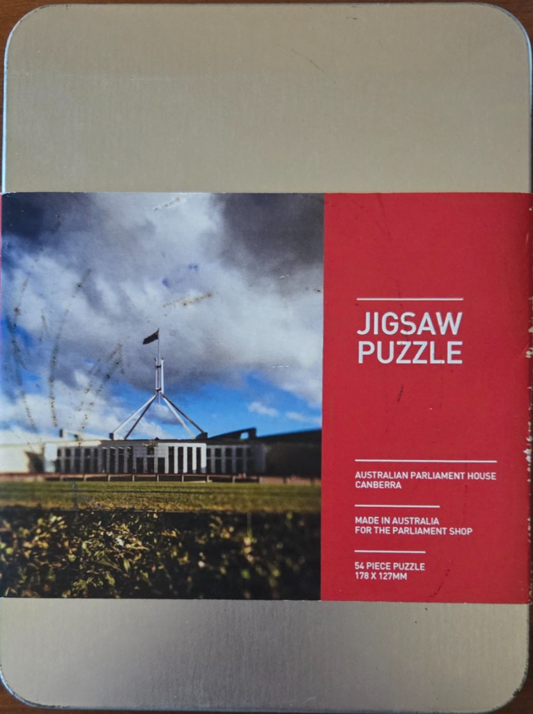 A photograph of the Australian Parliament House in Canberra beneath a partly cloudy blue sky.