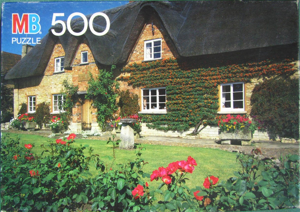 A charming English cottage with a thatched roof, surrounded by rose bushes and a vibrant green lawn.