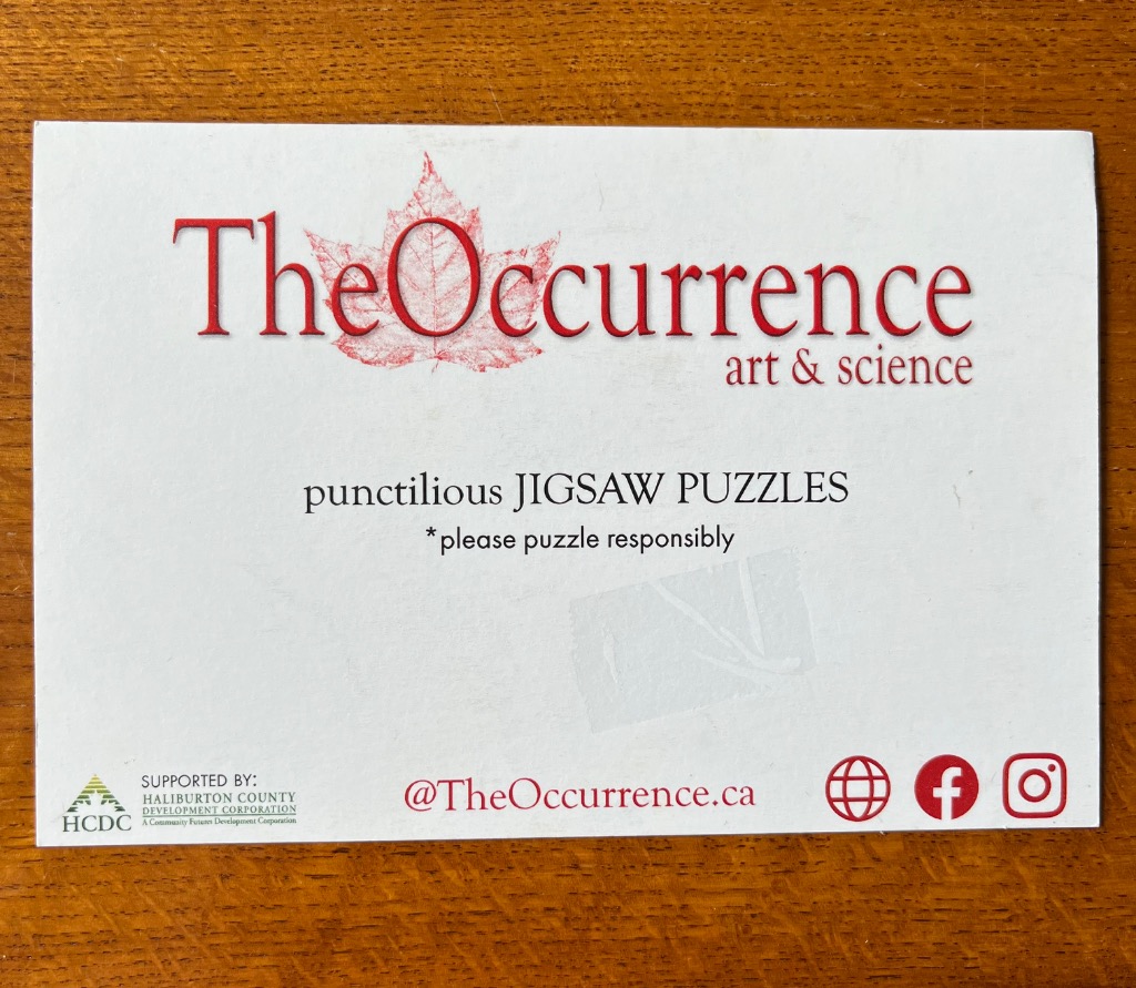 White card with red logo text featuring a maple leaf and contact information on a wooden surface.