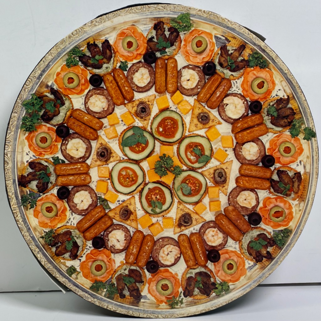 A top-down circular platter featuring an intricate, symmetric arrangement of party snacks and appetizers.