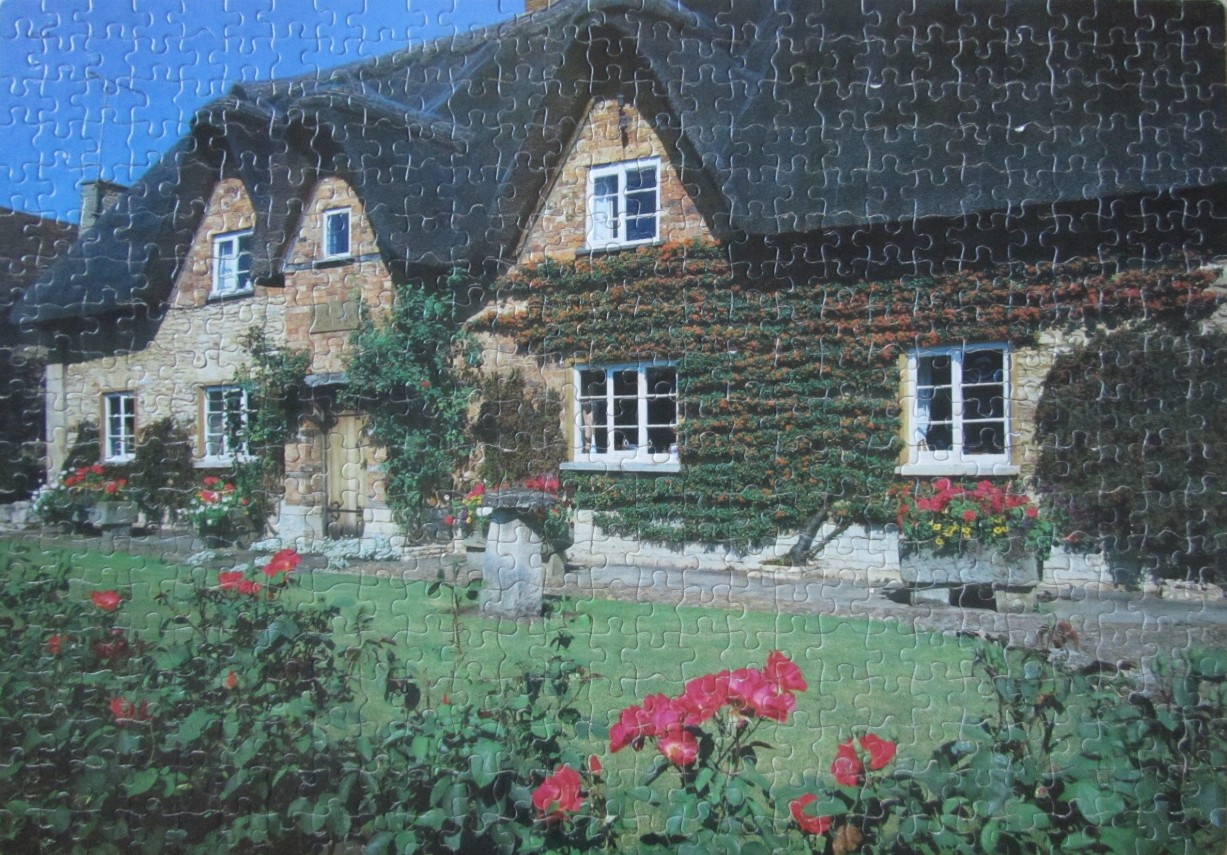 A stone cottage with a thatched roof and flower-filled garden under a clear blue sky.