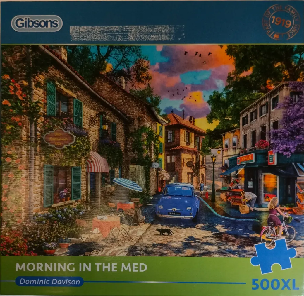 A charming Mediterranean village street scene at sunset with a blue vintage car, a cyclist, and stone buildings.
