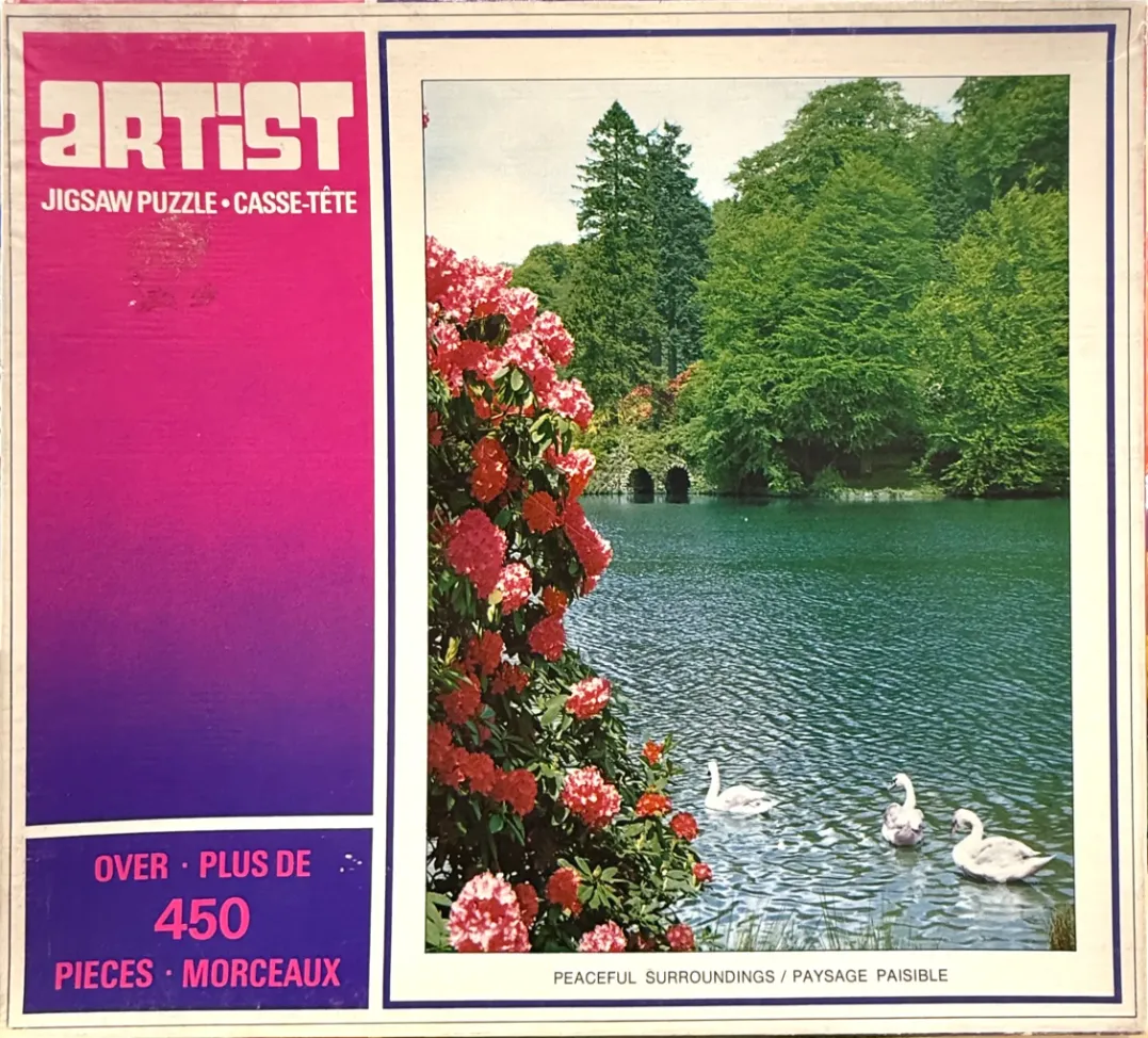 A peaceful landscape featuring a pond with three swans in front of a blooming rhododendron bush and a stone bridge.