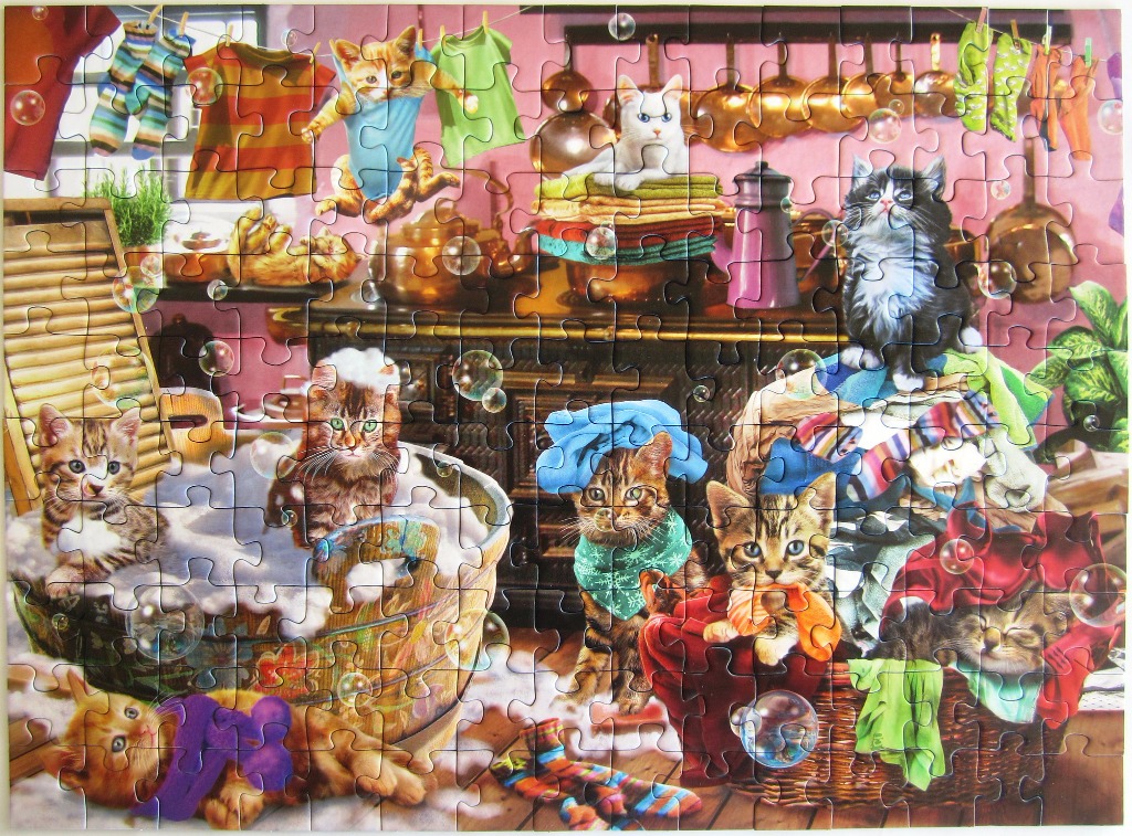 An illustration of many kittens playing in a laundry room filled with bubbles, colorful clothing, and baskets.