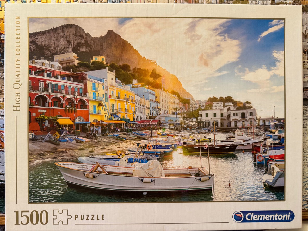 A scenic photograph of the harbor in Capri with colorful buildings and anchored boats at sunset.