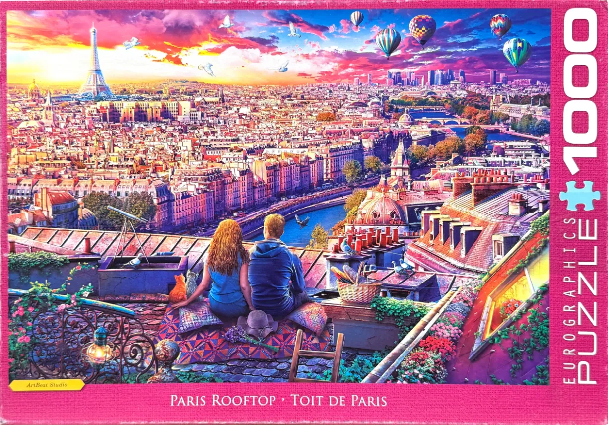 A couple sits on a Parisian rooftop overlooking the city at sunset with hot air balloons in the sky.