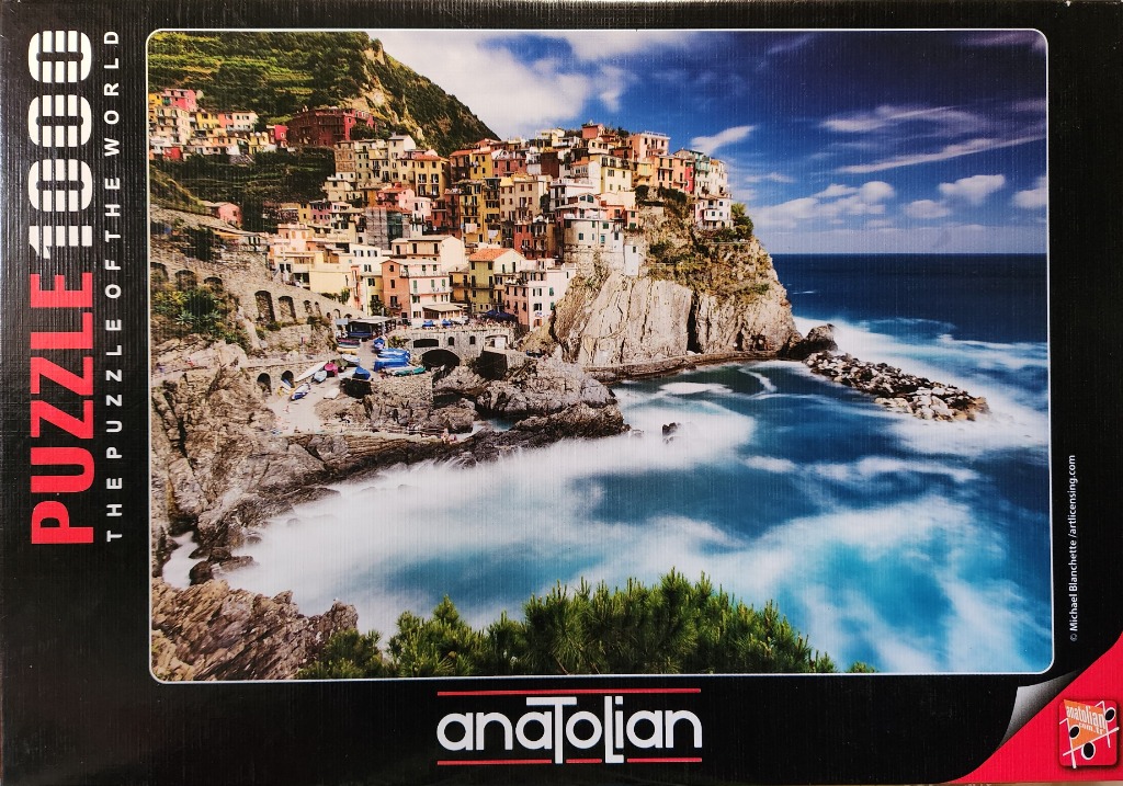 Coastal Italian village of Manarola perched on rocky cliffs above a turquoise sea with surf crashing against the shore.