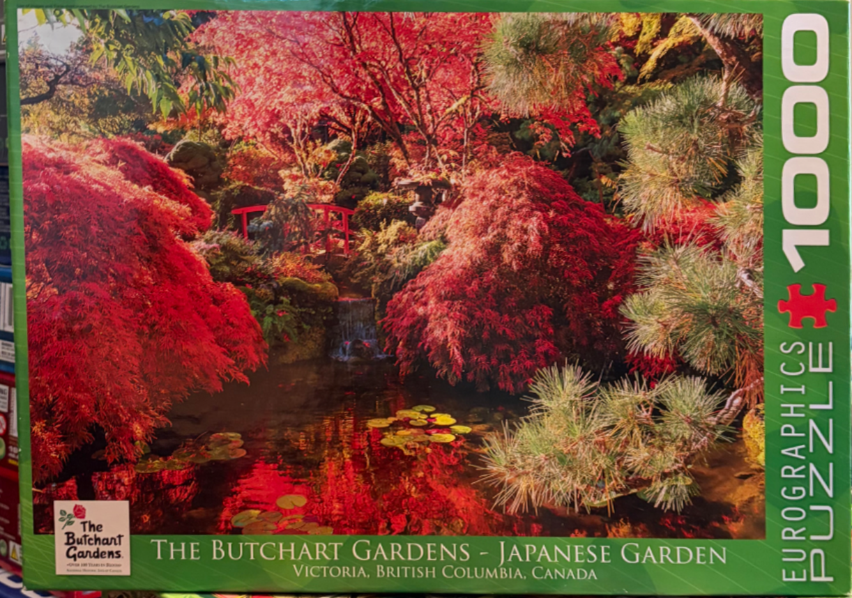A lush Japanese garden in autumn with vibrant red maples, a pond, and a small bridge.