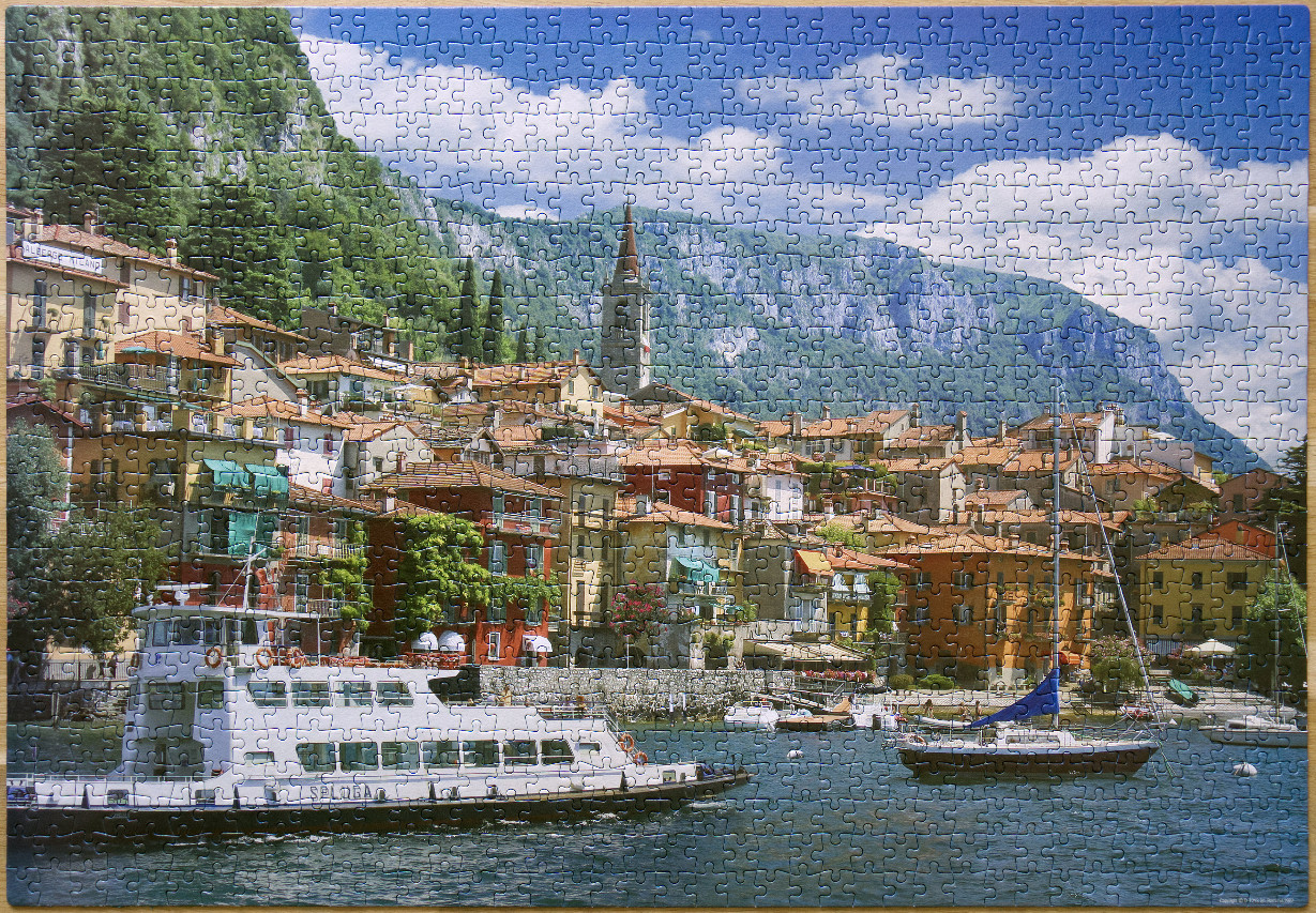 A colourful hillside village overlooking a lake with a passenger ferry and sailboat in the foreground.