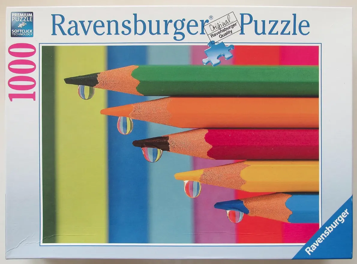 A stack of five colorful pencils with water droplets on the tips against a multicolored striped background.