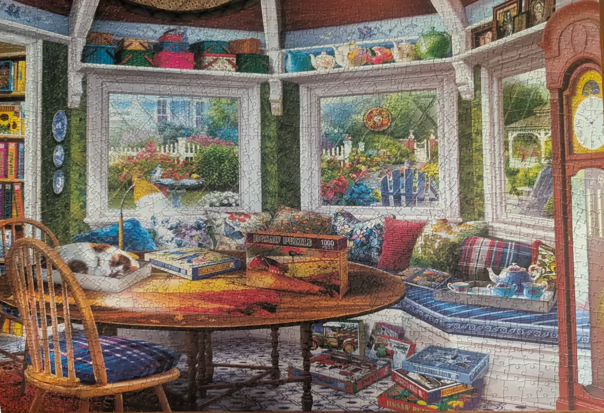 A cozy sunroom interior featuring a round table, a window seat with cushions, and garden views.