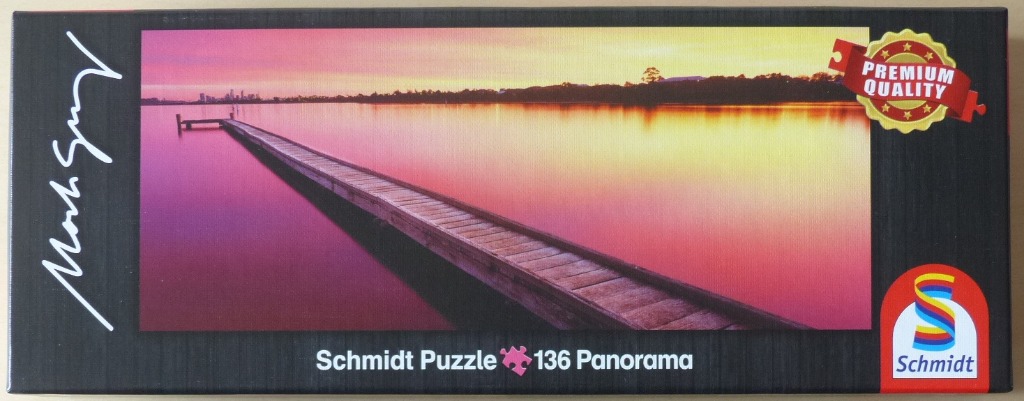 A panoramic photograph of a wooden pier stretching into calm water during a vibrant pink and orange sunset.