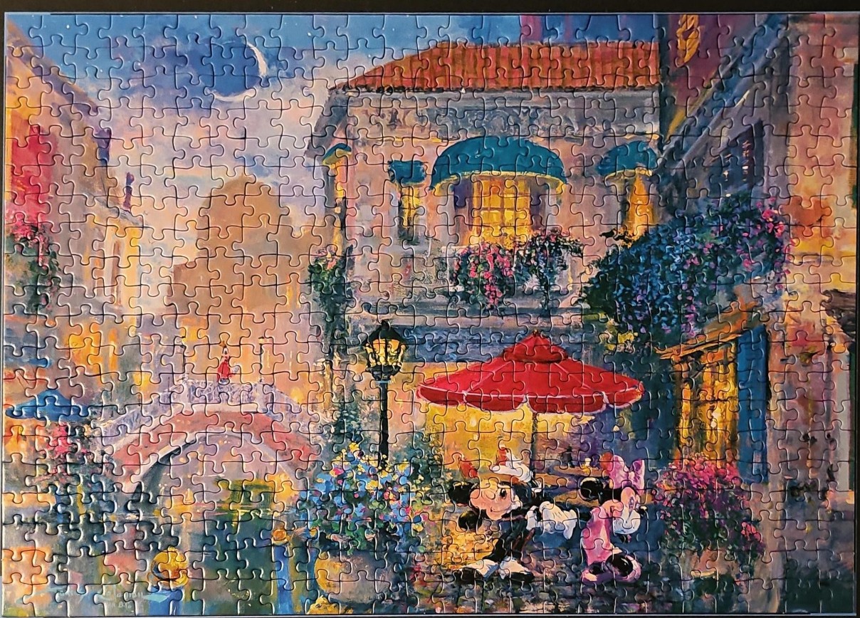 Mickey and Minnie Mouse on an evening stroll in a charming European-style town square with a canal bridge.