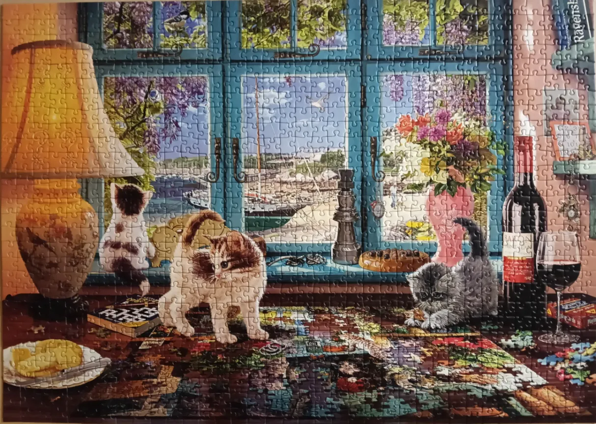 Three kittens playing on a cluttered desk in front of a window overlooking a harbor.