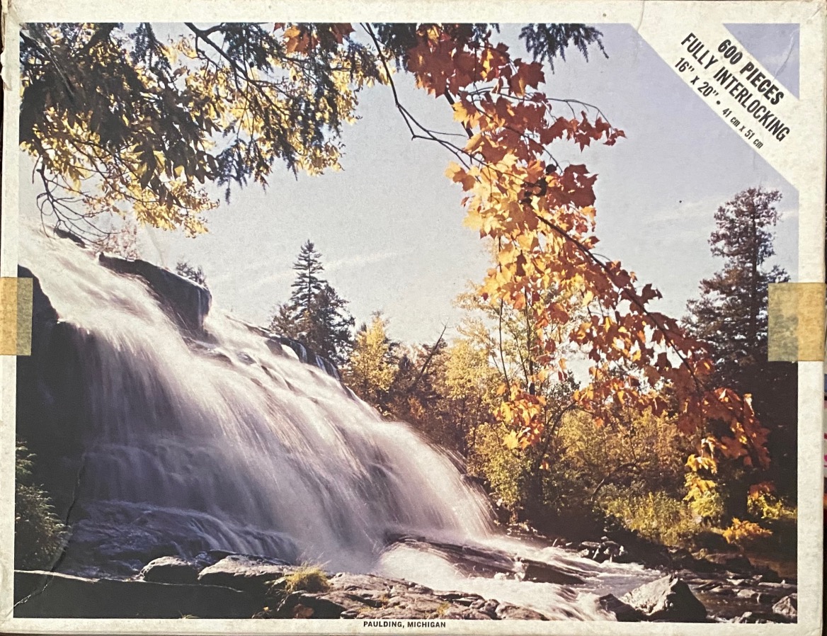 A waterfall cascades over dark rocks surrounded by autumn foliage in Paulding, Michigan.