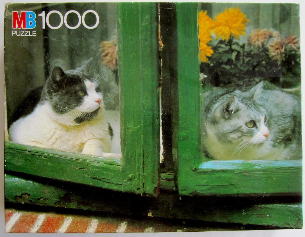 Two cats looking out from behind a weathered green window frame
