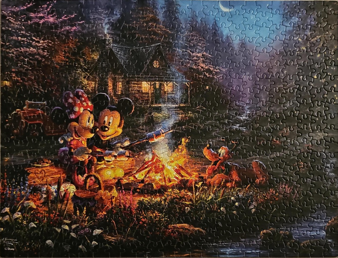 Mickey and Minnie Mouse roasting marshmallows by a campfire in front of a rustic cottage at night.