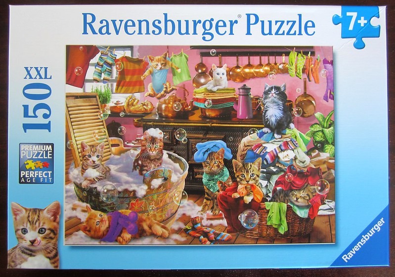 Several kittens playing in a laundry room filled with soap bubbles, copper cookware, and colorful clothing.