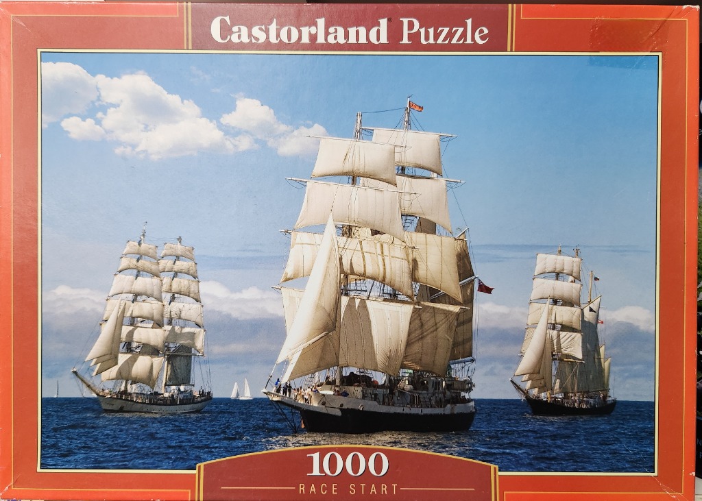 Three large tall ships with white sails sailing on the ocean under a blue sky.