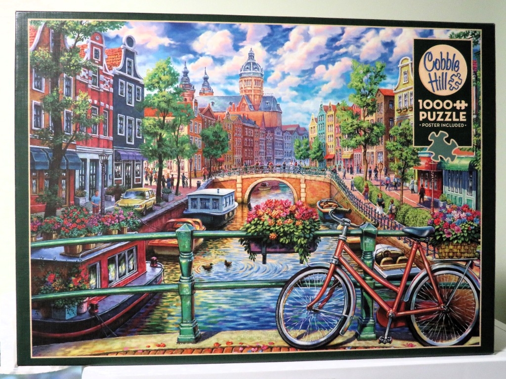 Painting of a canal scene in Amsterdam featuring historic buildings, a stone bridge, and a red bicycle in the foreground.