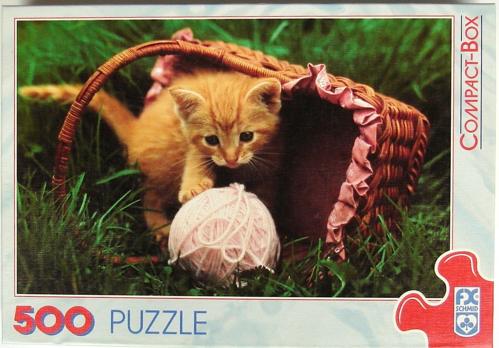 A cute orange tabby kitten playing with a pink ball of yarn inside a wicker basket in the grass.