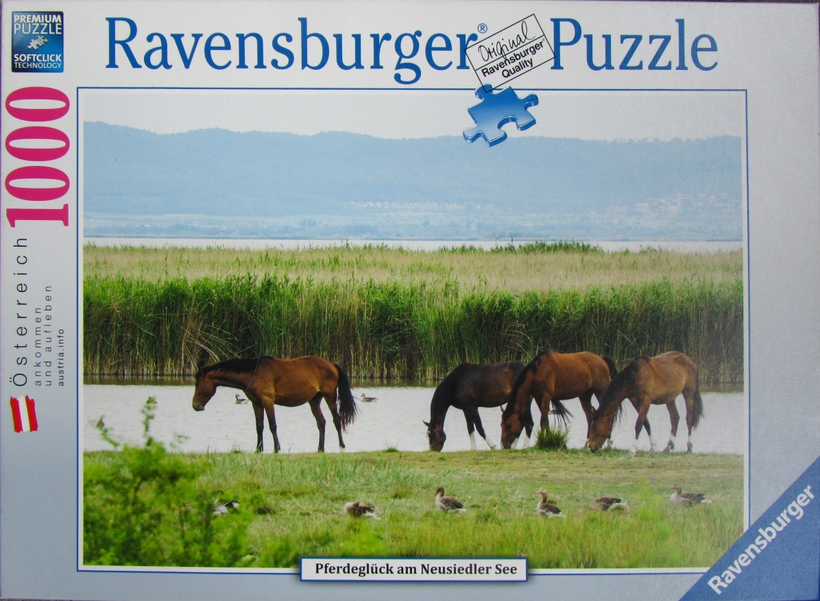 Four horses grazing near a lake in a grassy, reed-lined meadow with geese and distant hills.