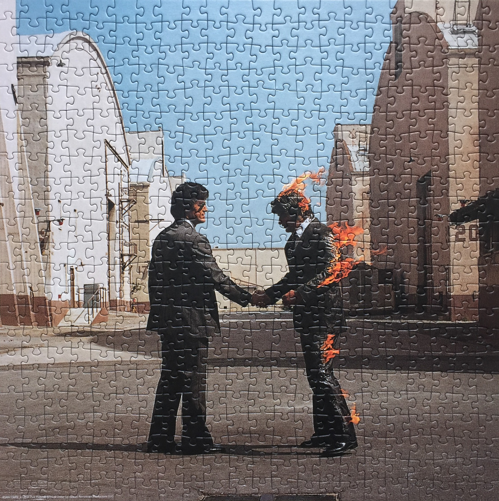 Two businessmen shaking hands in an industrial lot, one of whom is engulfed in flames.