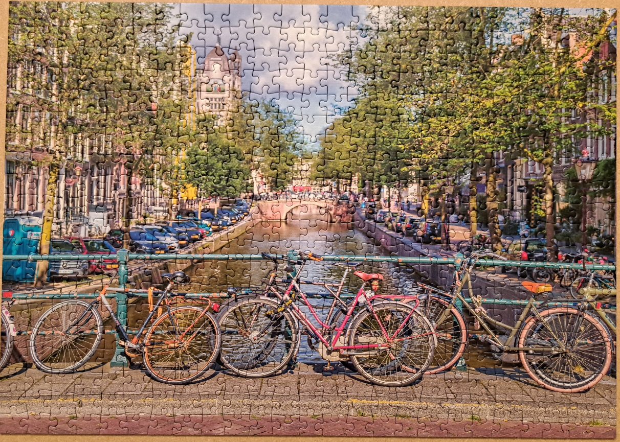 Bicycles parked on a bridge over a canal in Amsterdam lined with trees and traditional buildings.