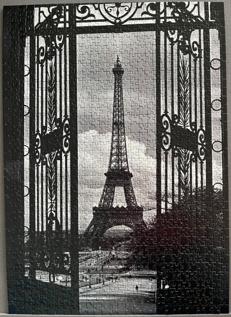A black and white photograph of the Eiffel Tower viewed through an ornate iron gate.